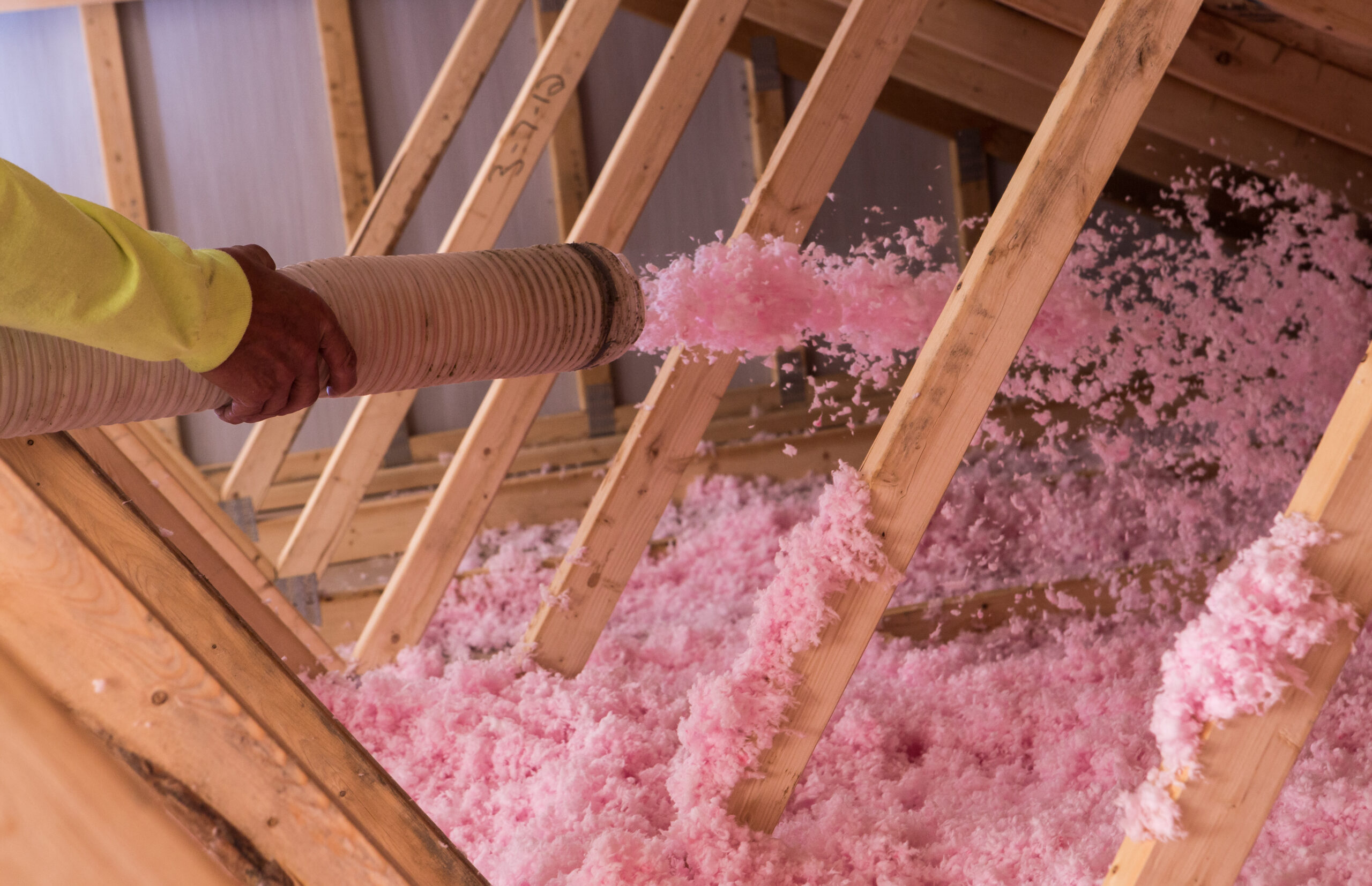 An installer blowing in fiberglass blown-in insulation in an attic